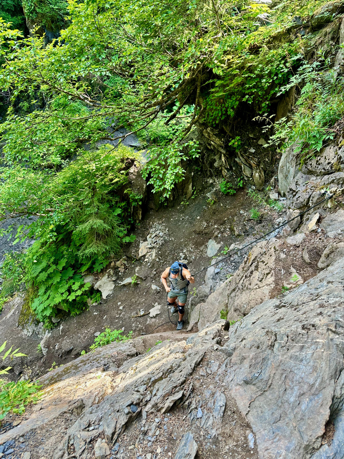 Coop (aka The Productive Adventurer) using ropes to climb up a steep rock on the Chutes and Ladders hike in Girwood Alaska