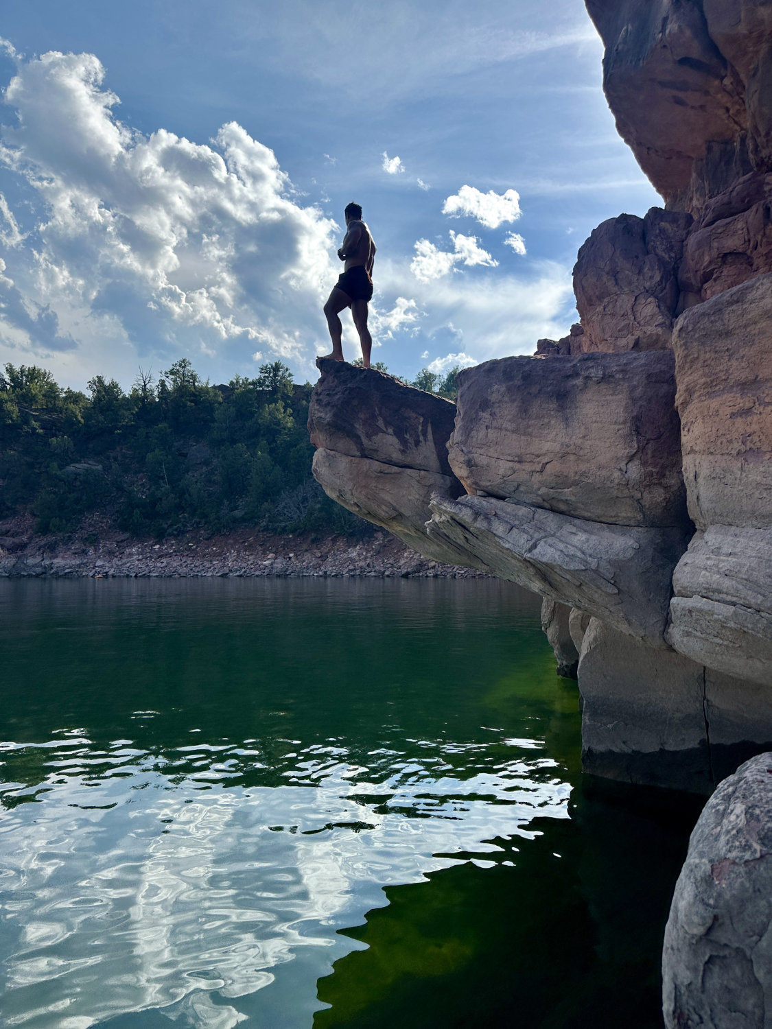 Cooper mid-air during a cliff jump at Flaming Gorge, showcasing the thrill and height of the jump against the backdrop of red cliffs and blue water