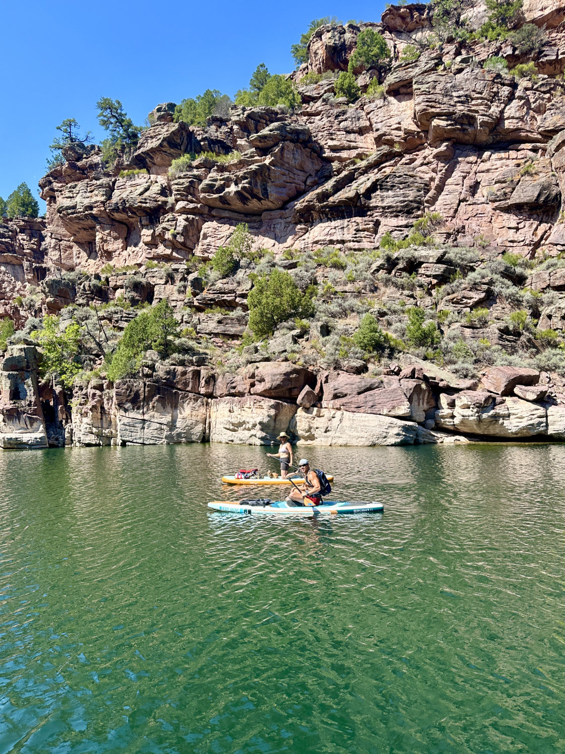 Kristin and Cooper paddle boarding together near the towering red cliffs of Flaming Gorge, highlighting the scale of the landscape and the serenity of the water