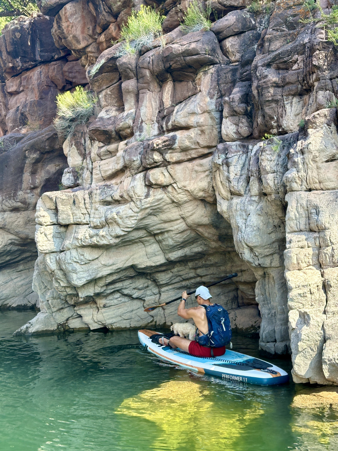 Cooper paddle boarding near towering red cliffs at Flaming Gorge, showcasing the stunning contrast between the blue water and the rugged landscape