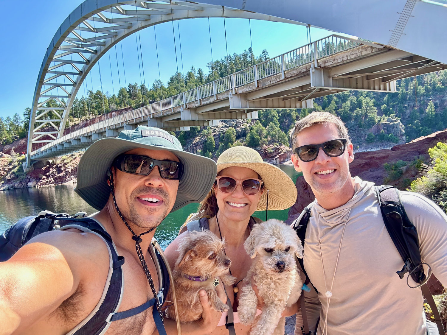 Group of friends and their dogs posing on a scenic bridge overlooking Flaming Gorge, with stunning red rock formations and blue water in the background