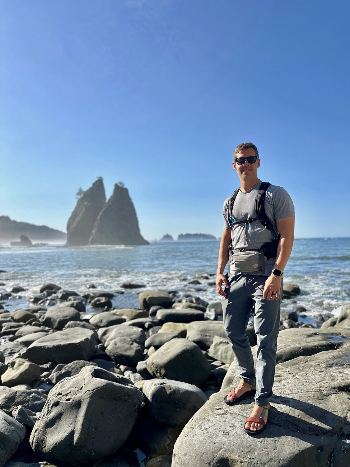 Portrait of Mark standing on large rocks with Sea Stacks in the backround. Photographed at Rialto Beach in Olympic National Park.